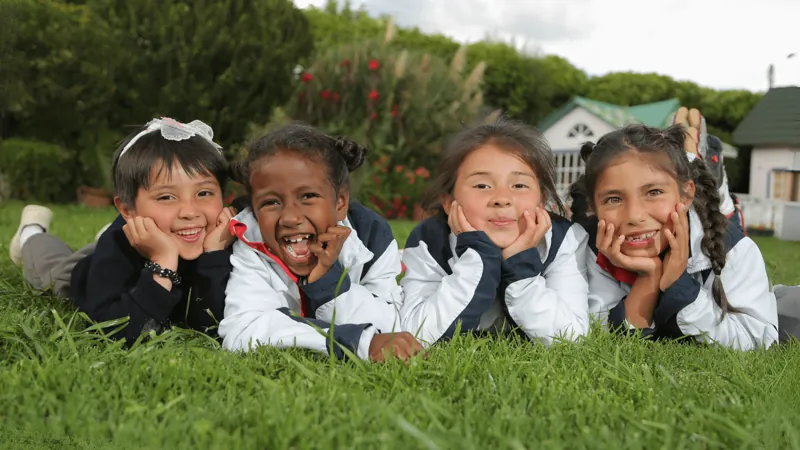 Cuatro niñas con uniforme escolar acostadas en el pasto, sonriendo